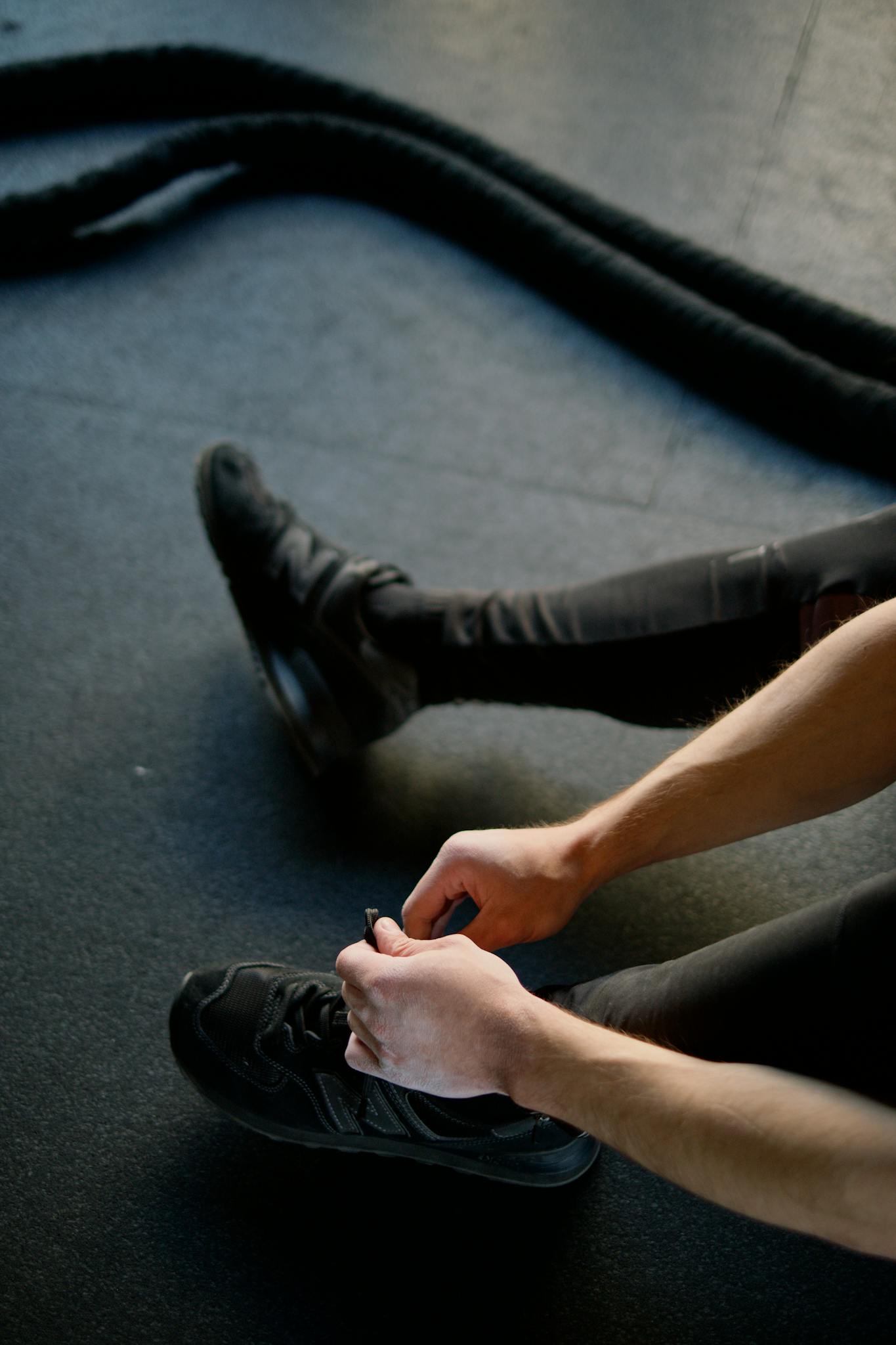 Person tying shoes in gym with battle ropes, ready for intense fitness session.