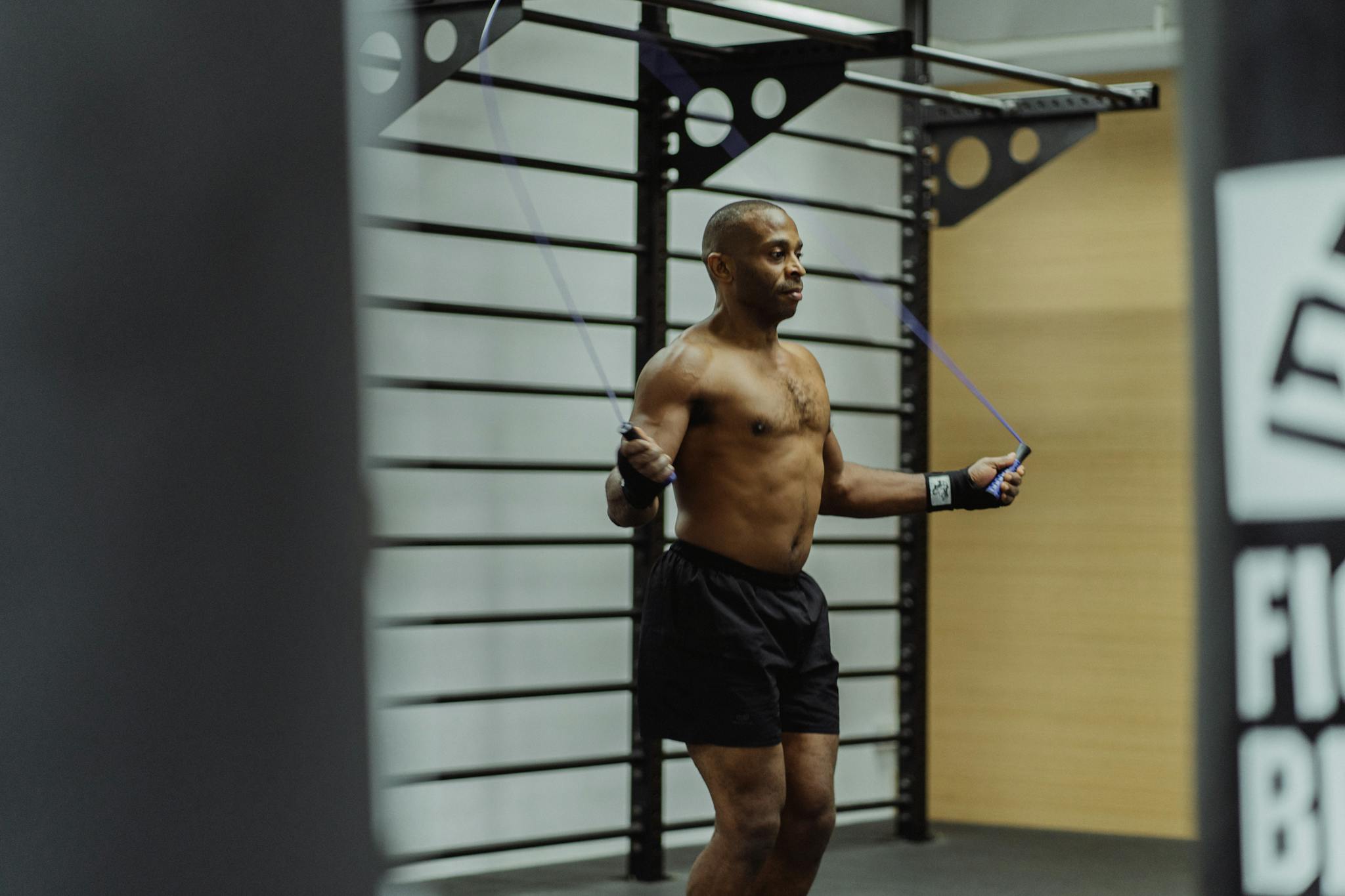 Shirtless man jumping rope indoors, focusing on fitness and training.