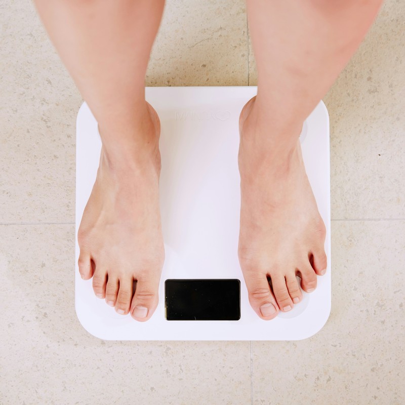 Person checking scale and fitness tracker for weight management