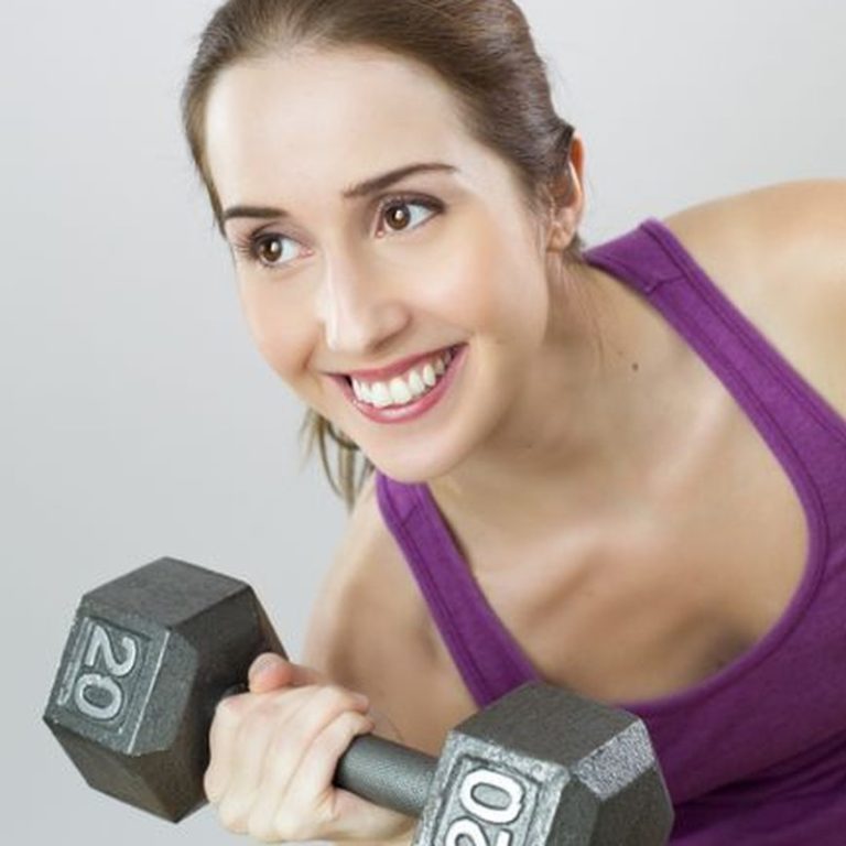 Young woman exercises with 20 lb dumbbell, showing strength and positivity.