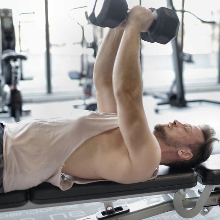 Active man engaged in strength training with dumbbells in a modern gym setting.
