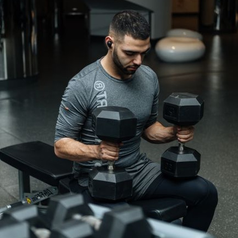 Adult man lifting dumbbells in a gym, focused on strength training workout.