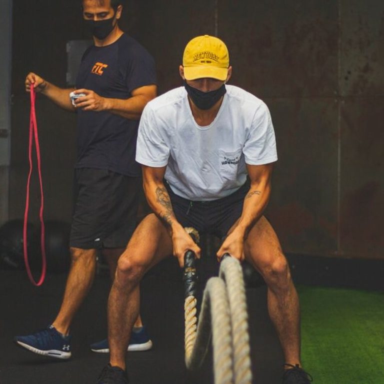 Two men engaged in a dynamic workout using battle ropes and resistance bands indoors.
