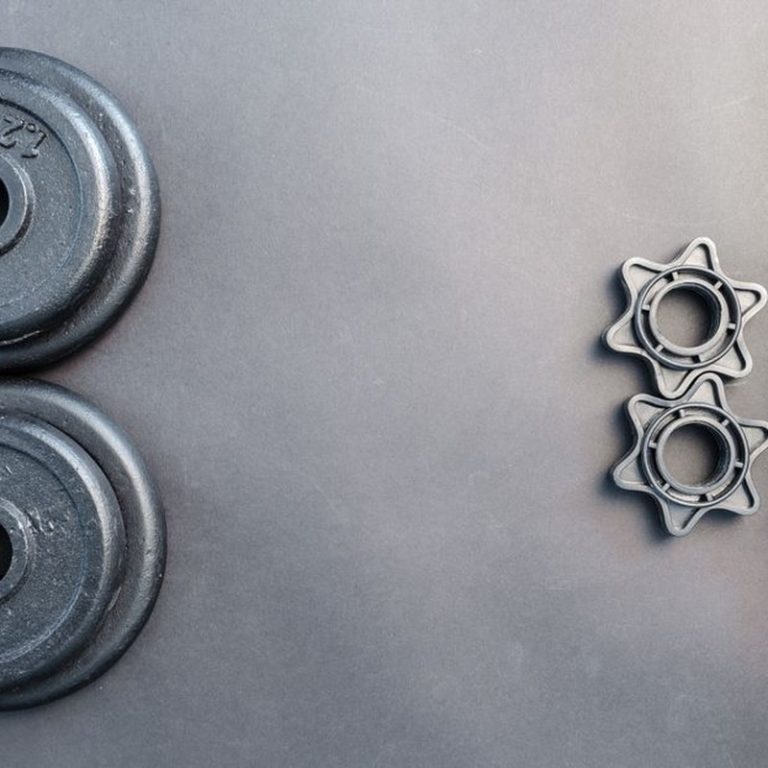 Barbell and two dumbbell weights arranged on a neutral gray surface.