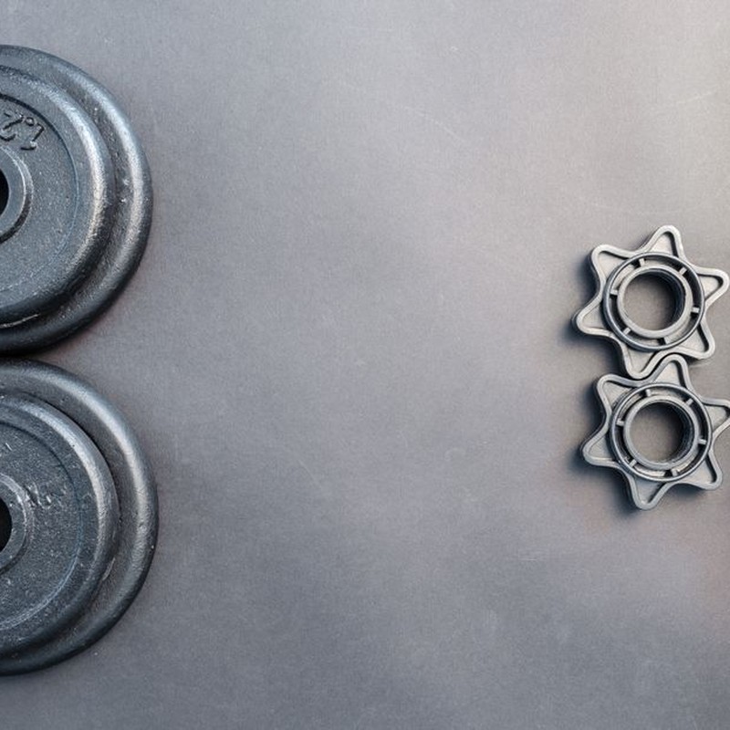 Barbell and two dumbbell weights arranged on a neutral gray surface.
