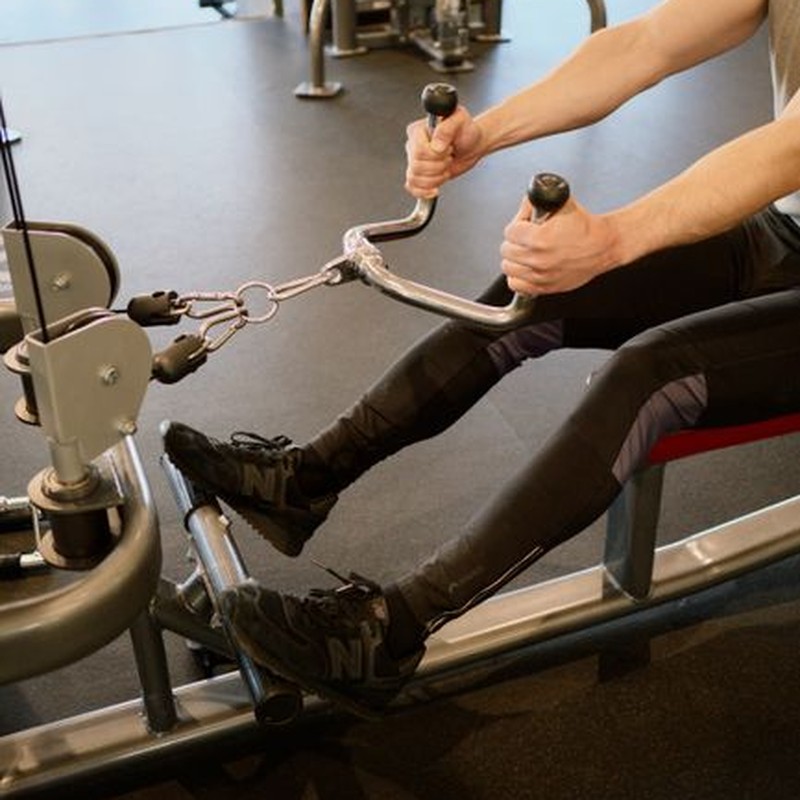 Adult male working out on a rowing machine in a modern fitness gym, emphasizing strength training.