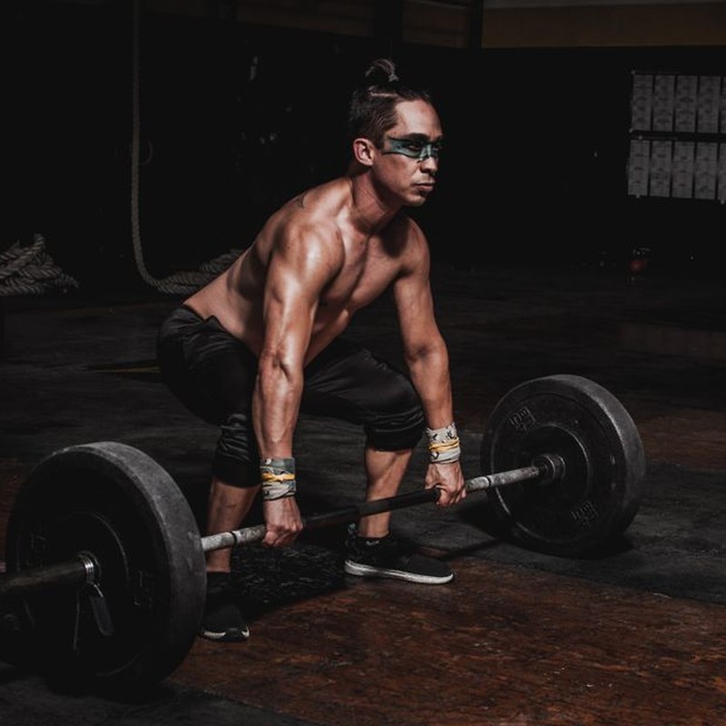 Strong athlete lifting heavy barbell in a dimly lit gym, showcasing strength and determination.