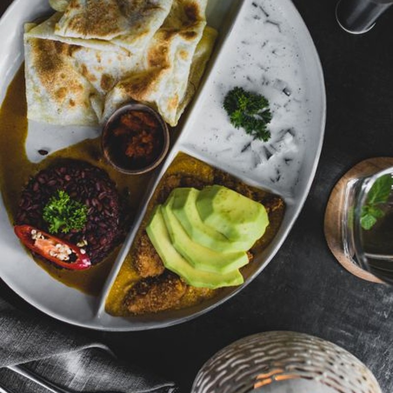 Top view of plate with red rice and roti bread served with sauces and avocado in cozy restaurant