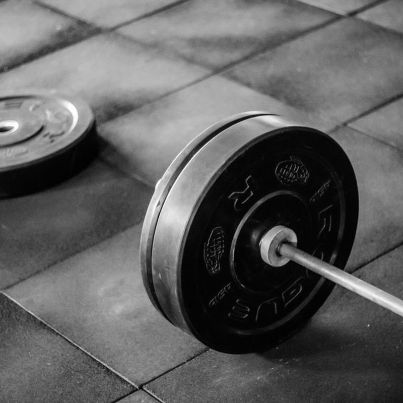 Grayscale image of heavy gym barbell and weights on rubber mat flooring.
