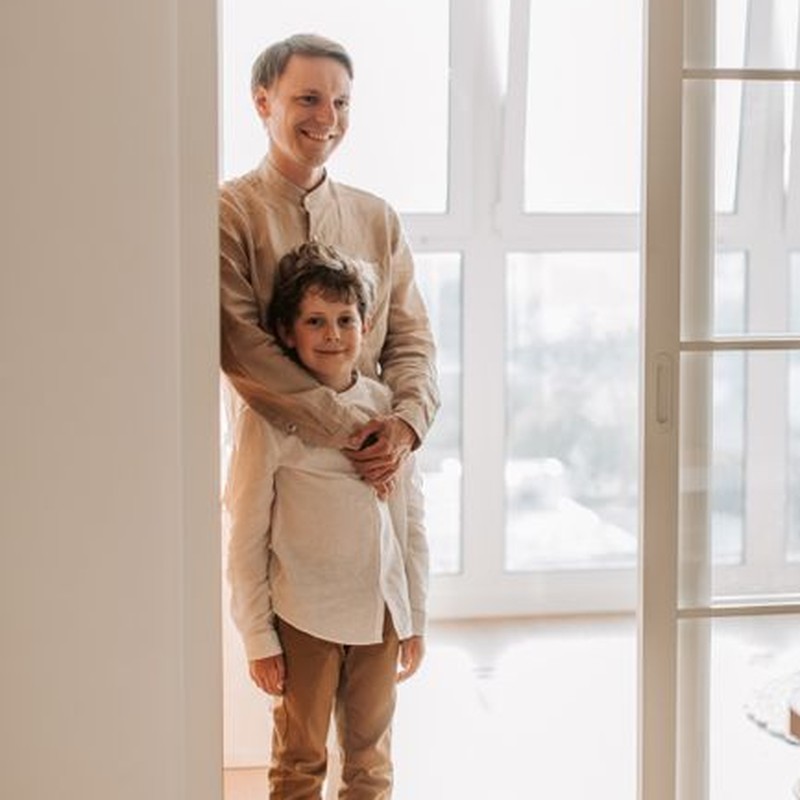 A cheerful father and son duo standing together sharing a warm embrace indoors.