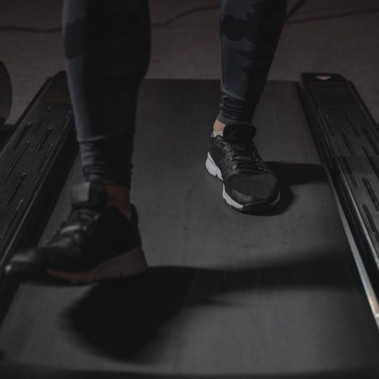 Feet running on treadmill in gym. Focus on black sneakers. Fitness and cardio exercise concept.