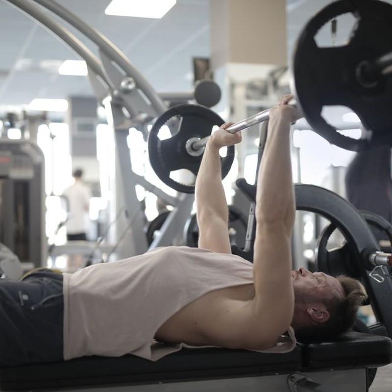 Side view of strong young sportsman in casual sportswear pressing heavy barbell on bench while intense training in modern fitness center
