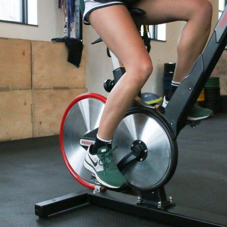 From below of anonymous crop person in shorts and sneakers exercising on stationary bike while training in gym