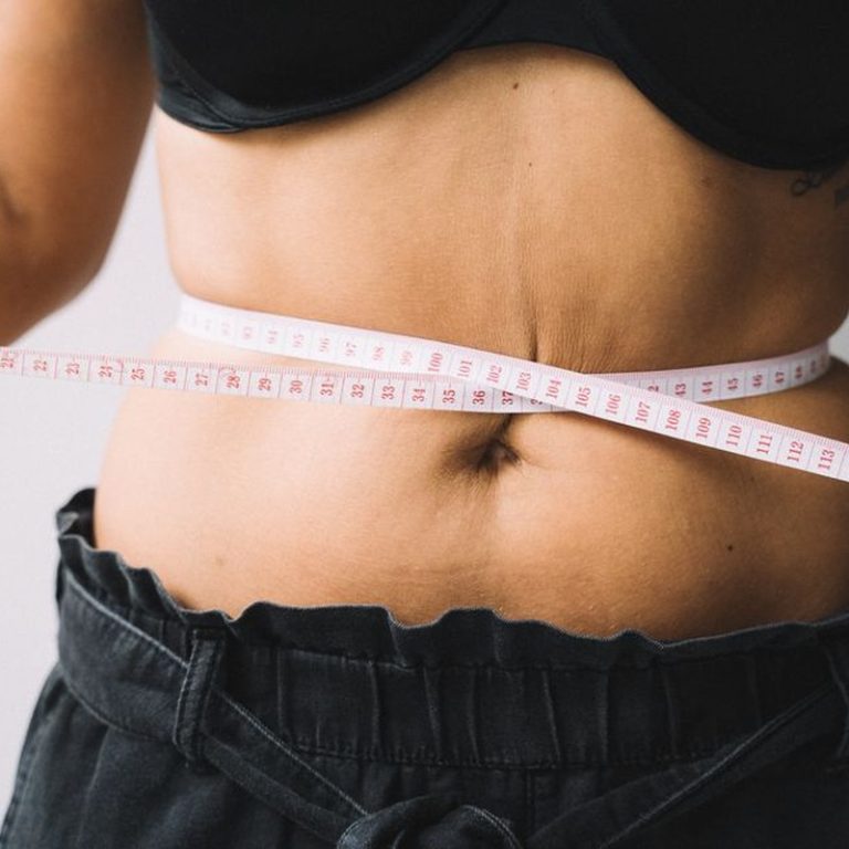 A person measuring their waist with a tape, symbolizing fitness and health goals.