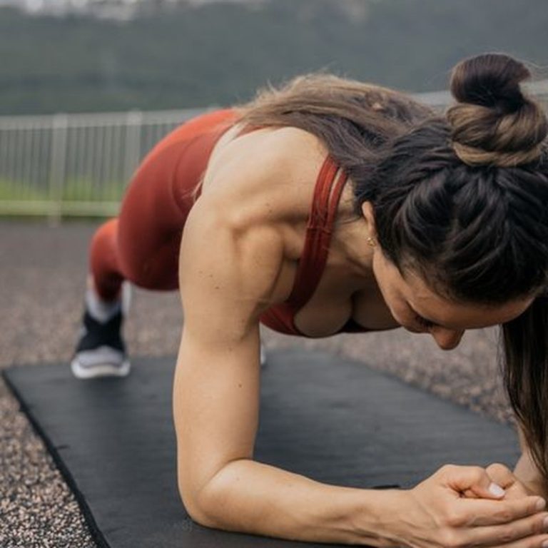 Focused woman doing a plank exercise on a yoga mat with mountains in the background.