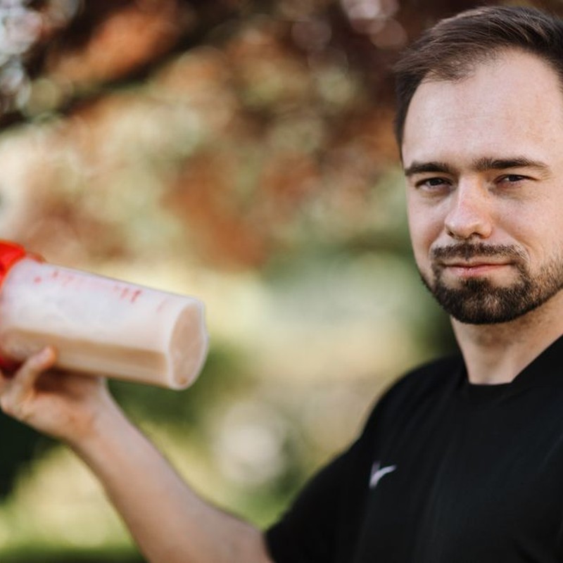 Adult man holding a protein shake outdoors during the day.
