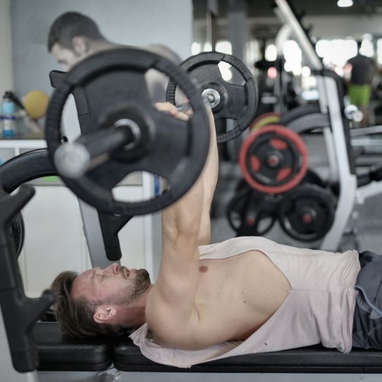 Side view of strong young sportsman in sportswear lying on bench and pressing heavy barbell doing chest exercise training in modern gym