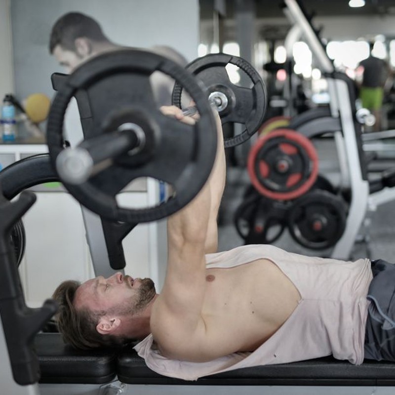 Side view of strong young sportsman in sportswear lying on bench and pressing heavy barbell doing chest exercise training in modern gym
