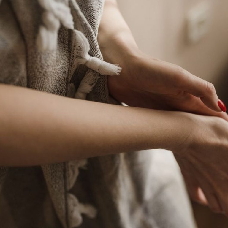 Elegant hands with red manicured nails touching the arm gently indoors.