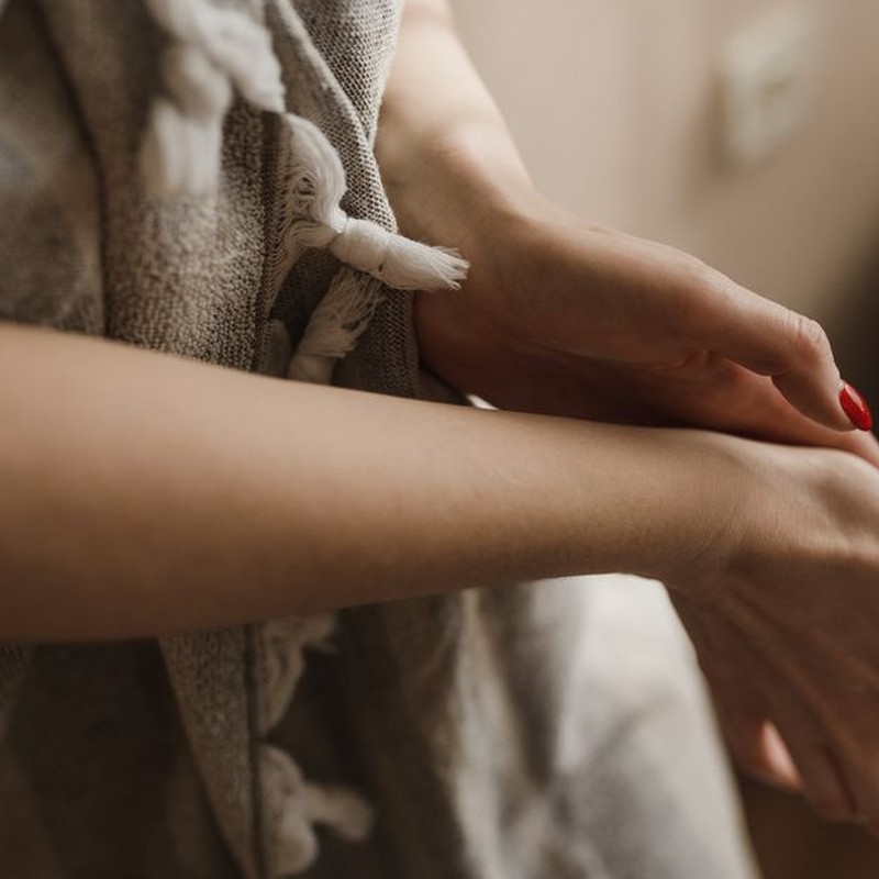 Elegant hands with red manicured nails touching the arm gently indoors.