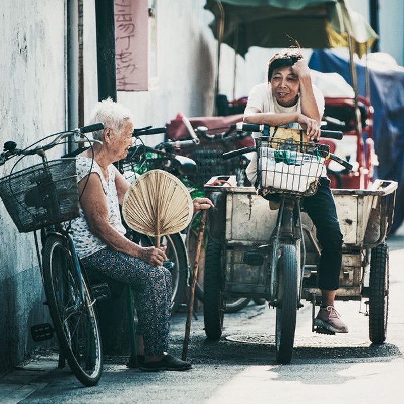 Two people on bikes sharing a moment on a sunny street in Beijing.