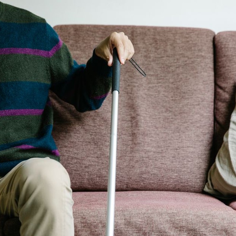 An adult sitting on a pink sofa holding a walking stick.