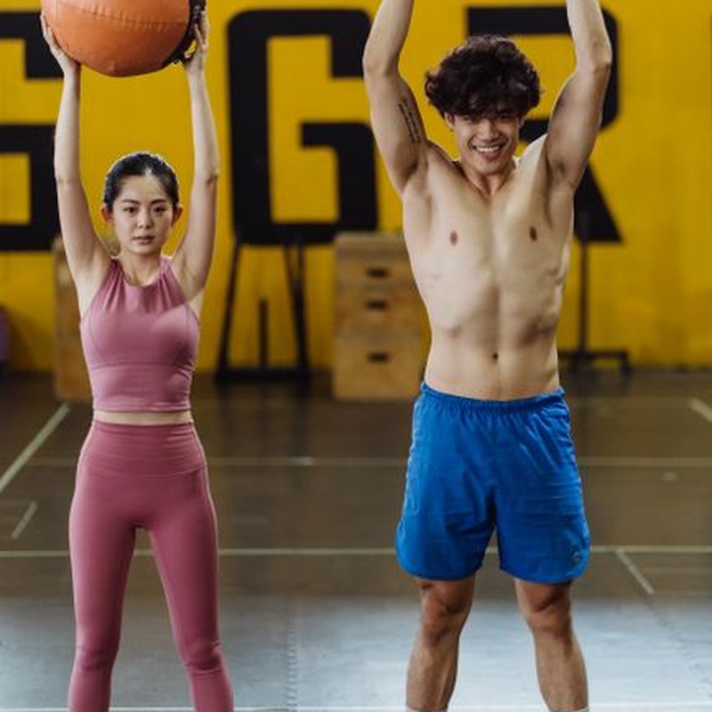 Asian couple in activewear working out with medicine balls indoors.