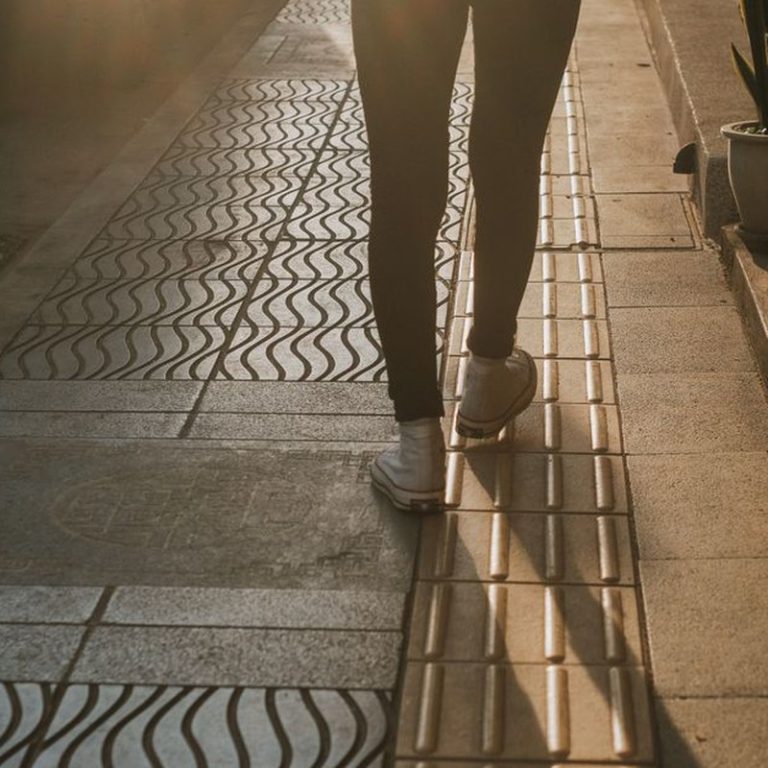 Silhouette of a person walking on a patterned street at sunset, highlighting urban fashion.