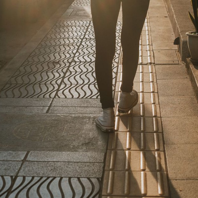 Silhouette of a person walking on a patterned street at sunset, highlighting urban fashion.