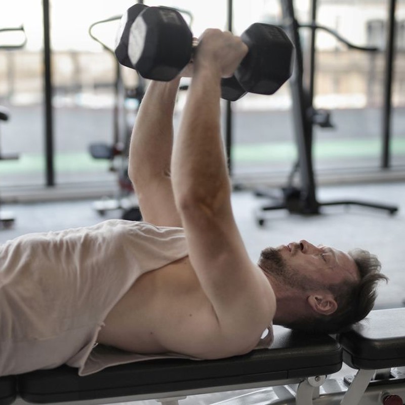 Man performing dumbbell press on bench indoors, focusing on muscle strength.
