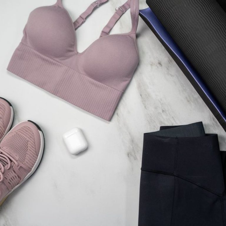 Pastel sports bra and sneakers with yoga mat and earphones on marble surface.