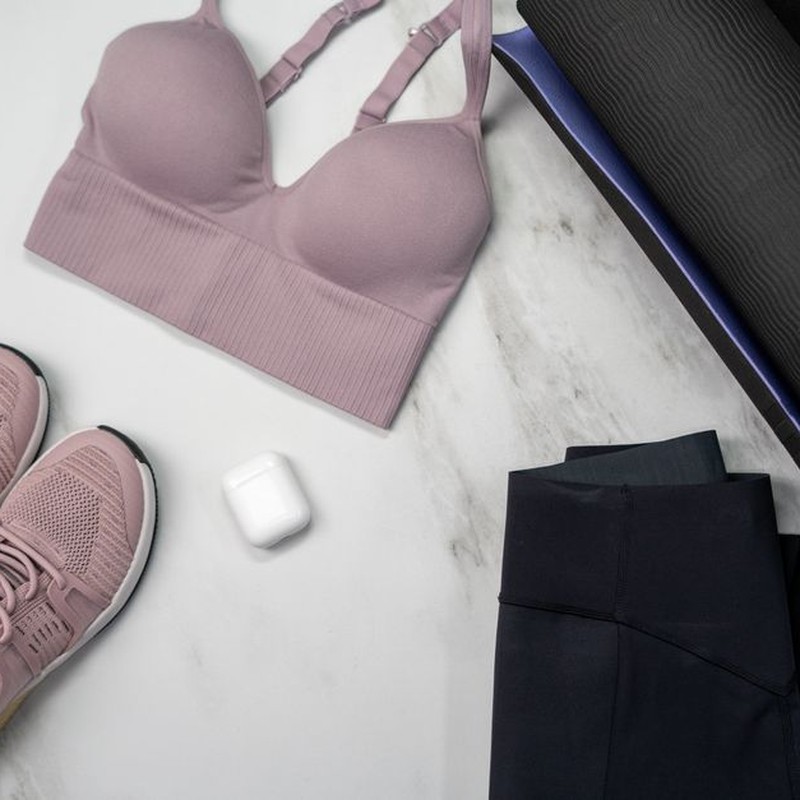 Pastel sports bra and sneakers with yoga mat and earphones on marble surface.
