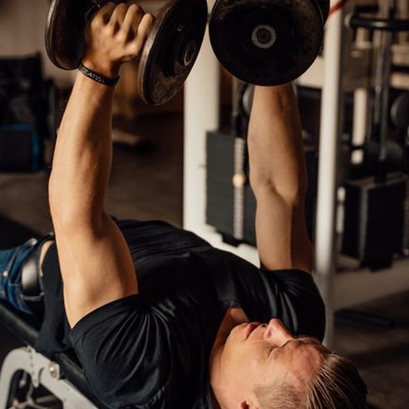 A muscular man lifting dumbbells while lying on a bench in the gym, showcasing strength training.