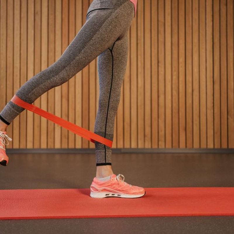 A woman performing leg exercises using a red resistance band on a yoga mat indoors.