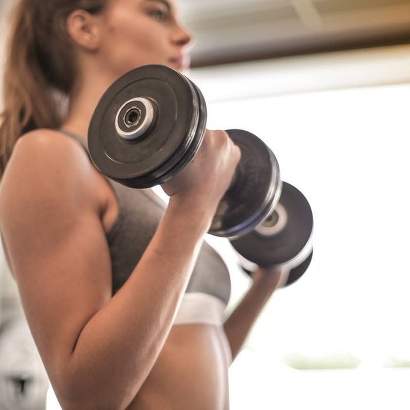 Focused woman lifting dumbbells in a bright gym, emphasizing strength and fitness.