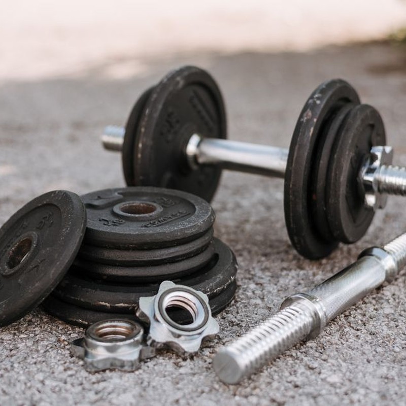 Heavy adjustable dumbbell near cast iron plates and hexagonal collars with stainless steel bar on pavement