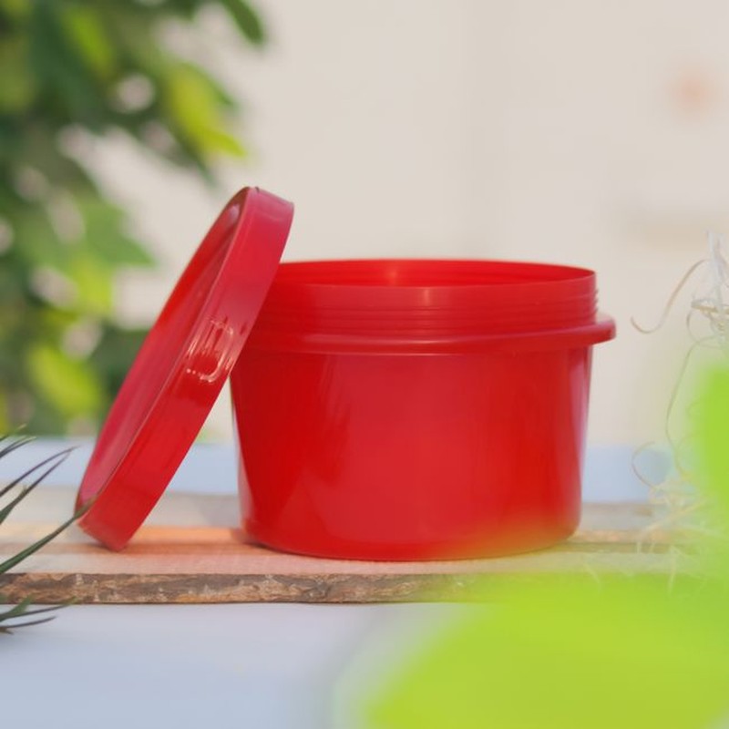 Open red plastic container with lid on a wooden board, ideal for storage solutions.