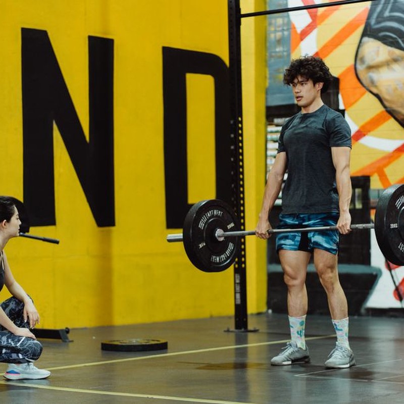 Man performing deadlift in the gym while female trainer watches, showcasing strength and fitness.