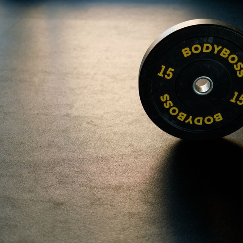 Black BodyBoss weight plate on gym floor, ideal for fitness and workout themes.