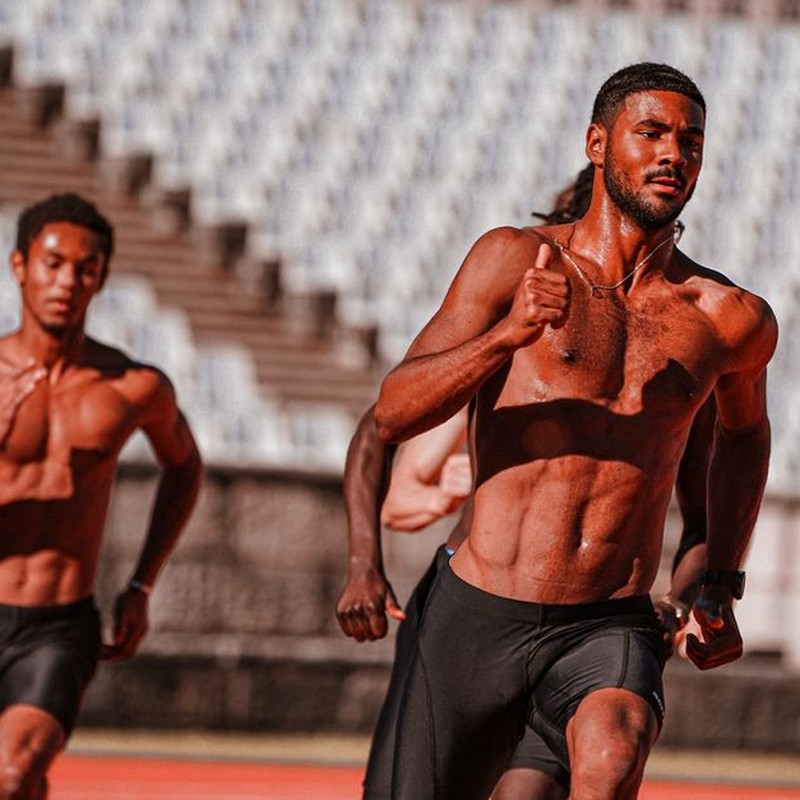 Shirtless male athletes displaying determination while sprinting on a sunny outdoor track.