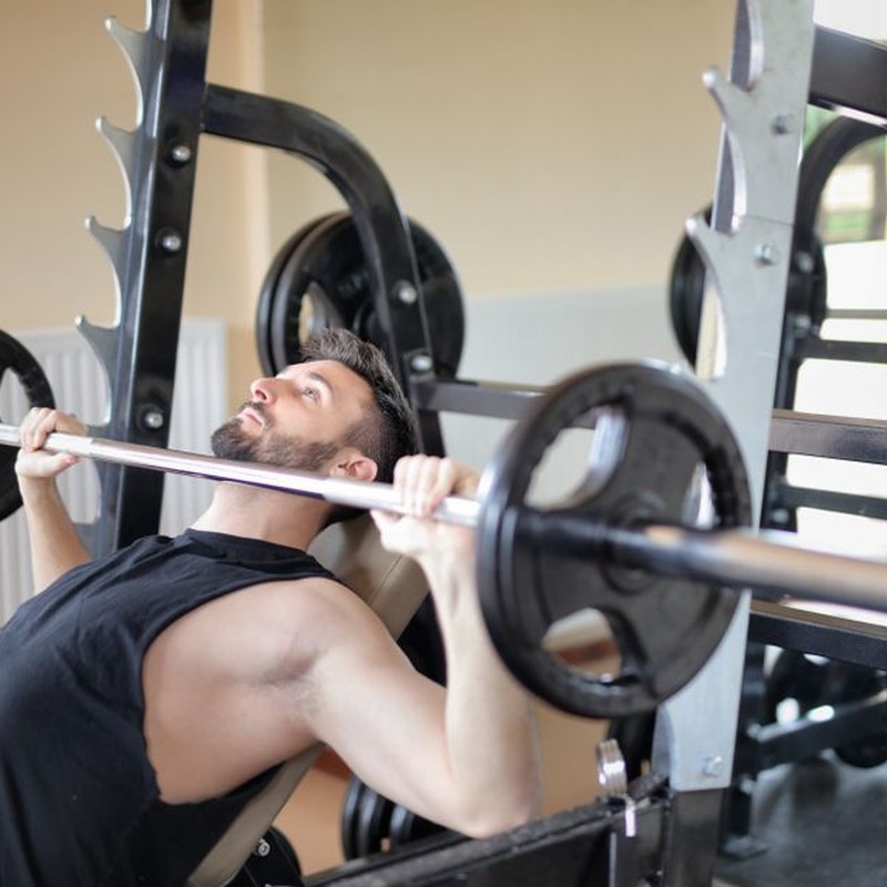 Adult man performing a bench press exercise at the gym, focusing on strength and muscle building.