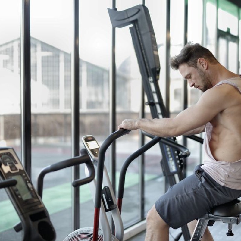 Side view of muscular male in sportswear training on exercise bike in modern fitness center