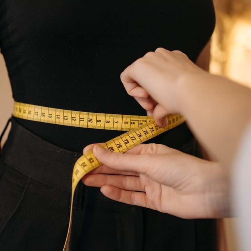 Close-up of tailor's hands measuring a person's waist with a yellow tape.