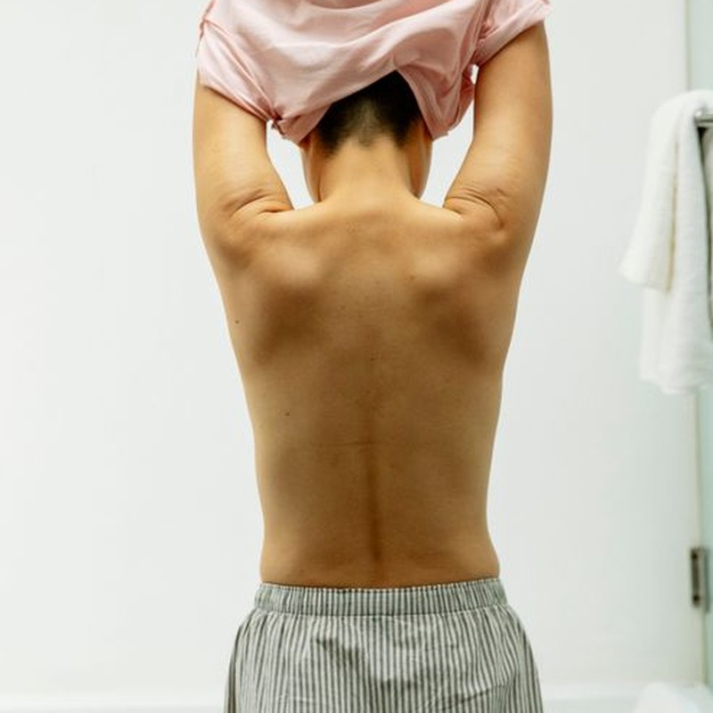Back view of anonymous person with short dark hair taking off t shirt in light room