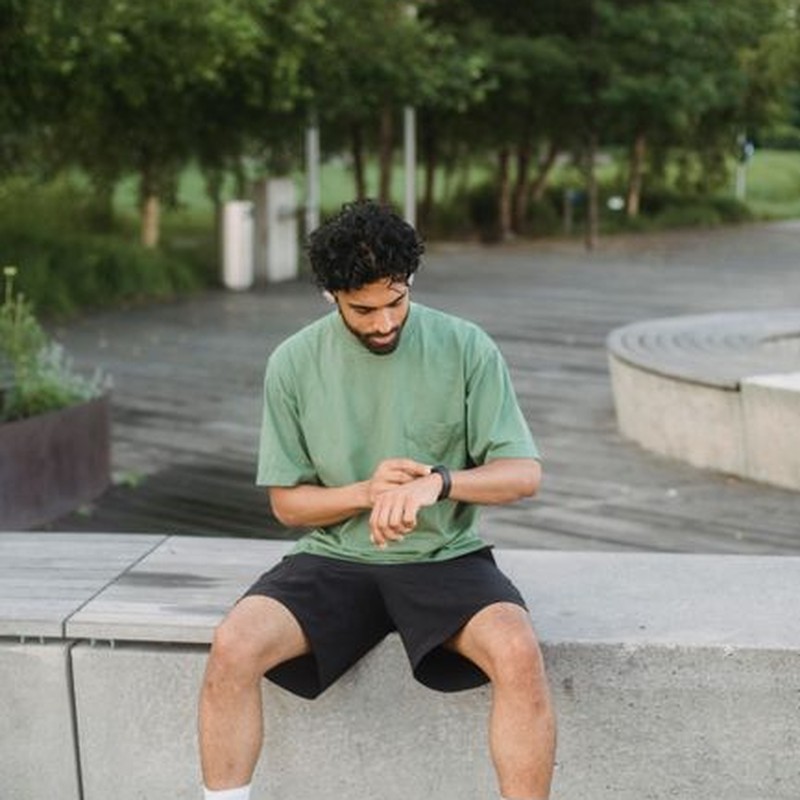 A man in casual sportswear checking his watch while sitting in a park.