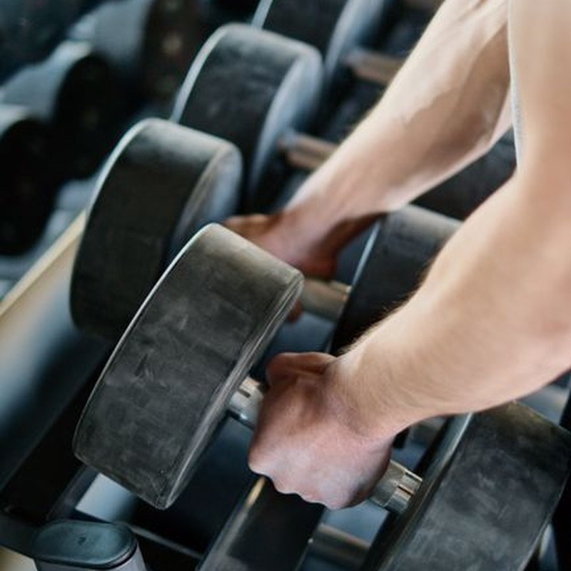 Focused shot of hands holding large dumbbells in a gym setting, showcasing strength workout.