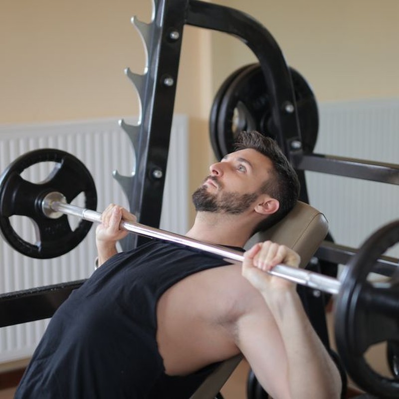Adult man performing bench press exercise with barbell in a gym setting, showcasing strength and fitness.