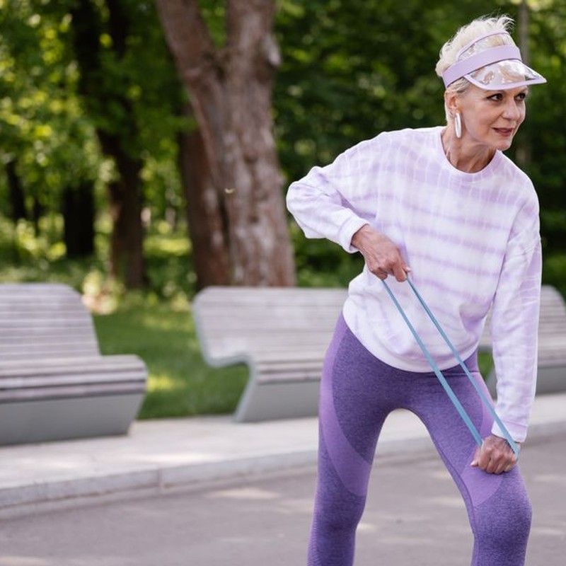 Senior woman performing outdoor exercise with a resistance band in a park setting.