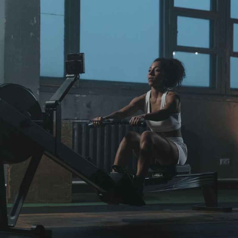 A woman working out on a rowing machine indoors, showcasing strength and focus.