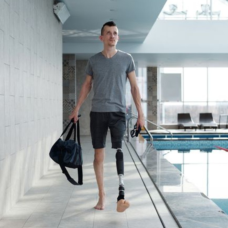 Man with prosthetic leg walking confidently by the swimming pool indoors.
